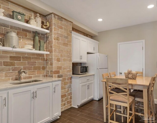 kitchen with white cabinets, white fridge, light stone countertops, and sink