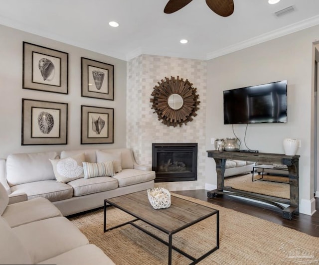 living room with wood-type flooring, a brick fireplace, ceiling fan, and ornamental molding