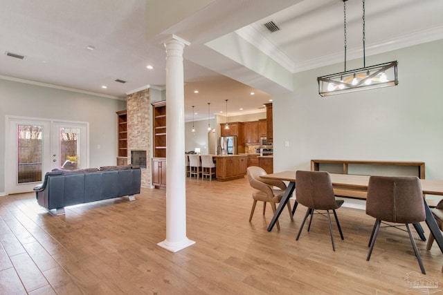 dining space featuring ornate columns, ornamental molding, light hardwood / wood-style floors, built in features, and a stone fireplace