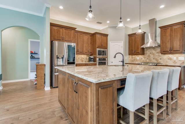 kitchen featuring stainless steel appliances, a spacious island, backsplash, hanging light fixtures, and wall chimney range hood