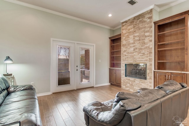 living room featuring a stone fireplace, light wood-type flooring, ornamental molding, french doors, and built in features