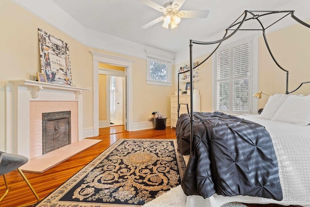 bedroom with a tile fireplace, ceiling fan, and hardwood / wood-style floors