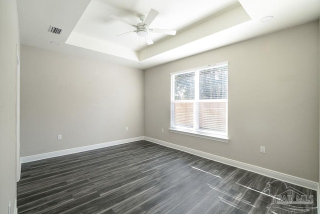 empty room featuring a tray ceiling, ceiling fan, and dark hardwood / wood-style flooring