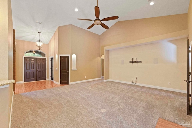 unfurnished living room featuring ceiling fan with notable chandelier, carpet, and high vaulted ceiling