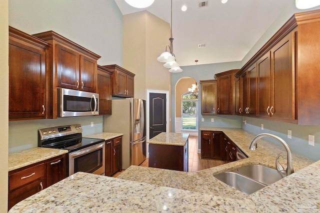 kitchen featuring light stone counters, stainless steel appliances, a high ceiling, decorative light fixtures, and sink