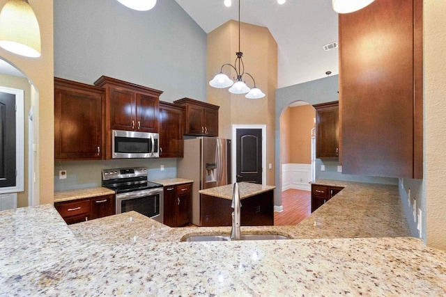 kitchen with appliances with stainless steel finishes, high vaulted ceiling, pendant lighting, hardwood / wood-style floors, and sink