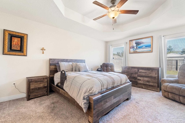 bedroom with a raised ceiling, baseboards, light carpet, and ceiling fan