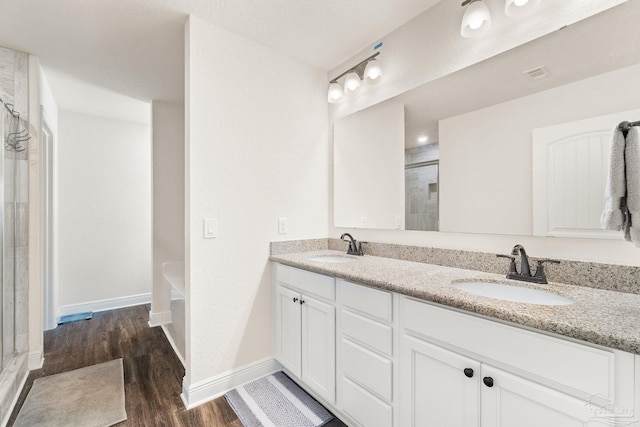 bathroom with double vanity, a stall shower, wood finished floors, a sink, and baseboards