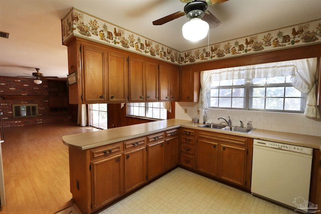 kitchen featuring ceiling fan, dishwasher, sink, a brick fireplace, and kitchen peninsula