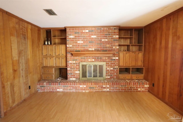 unfurnished living room with built in shelves, light hardwood / wood-style flooring, a brick fireplace, and wood walls