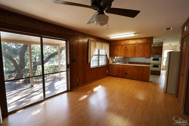 kitchen featuring white appliances, sink, wooden walls, light hardwood / wood-style flooring, and ceiling fan