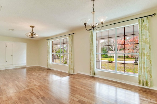 interior space featuring plenty of natural light, light hardwood / wood-style flooring, a textured ceiling, and an inviting chandelier