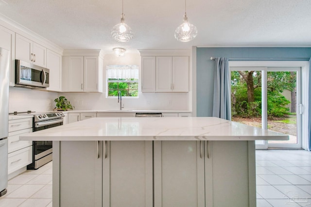 kitchen with sink, stainless steel appliances, light stone counters, pendant lighting, and white cabinets