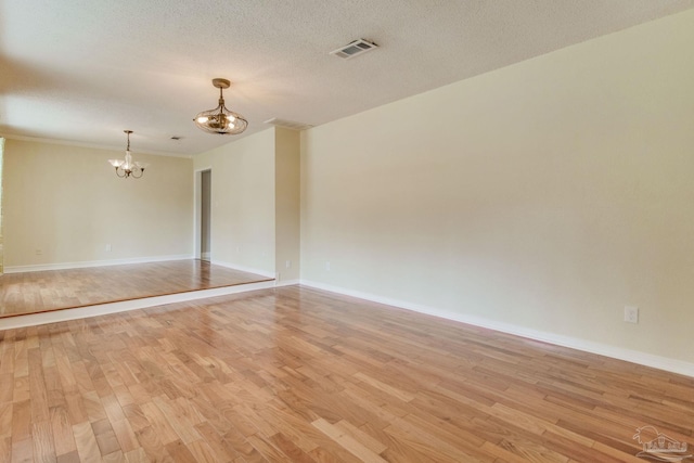 empty room featuring light hardwood / wood-style flooring, a textured ceiling, and an inviting chandelier