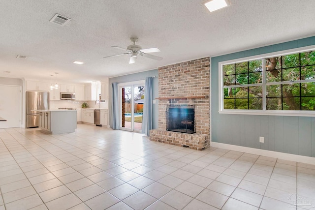 unfurnished living room with ceiling fan, light tile patterned floors, a textured ceiling, and a brick fireplace