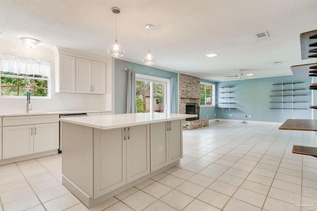 kitchen featuring a center island, sink, hanging light fixtures, a fireplace, and white cabinetry