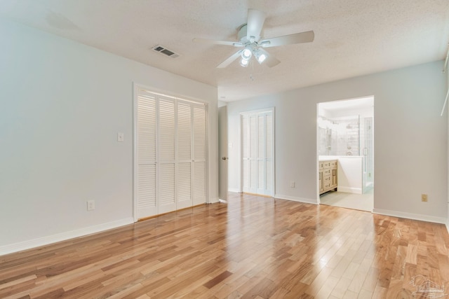 unfurnished bedroom featuring a textured ceiling, ceiling fan, light hardwood / wood-style flooring, and ensuite bath