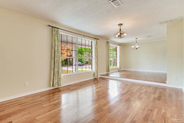 empty room featuring a textured ceiling, light hardwood / wood-style flooring, and a chandelier