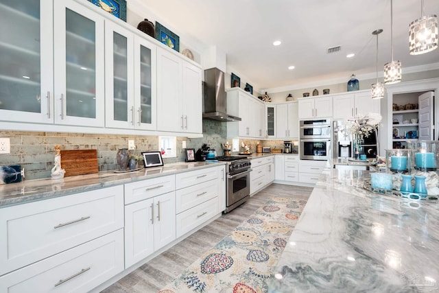 kitchen with light stone counters, appliances with stainless steel finishes, wall chimney exhaust hood, and white cabinetry