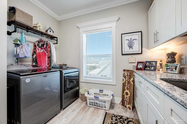 laundry area featuring cabinets, ornamental molding, washer and clothes dryer, and light hardwood / wood-style flooring