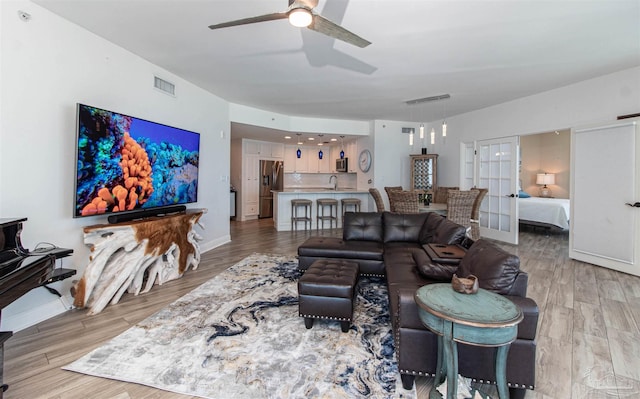 living room with sink, light hardwood / wood-style flooring, ceiling fan, and french doors