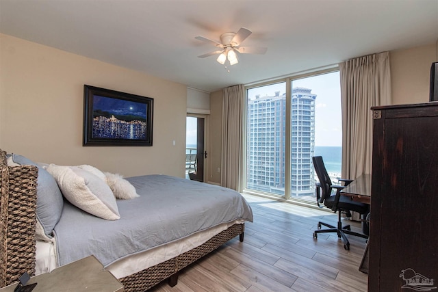 bedroom with light hardwood / wood-style floors, a water view, access to exterior, a wall of windows, and ceiling fan