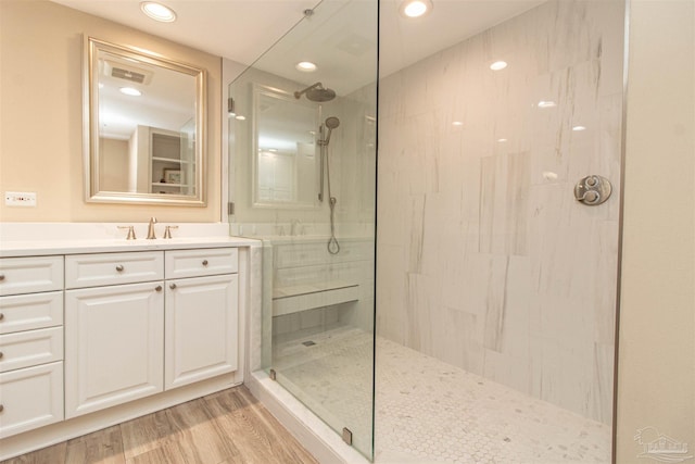 bathroom with wood-type flooring, a tile shower, and vanity