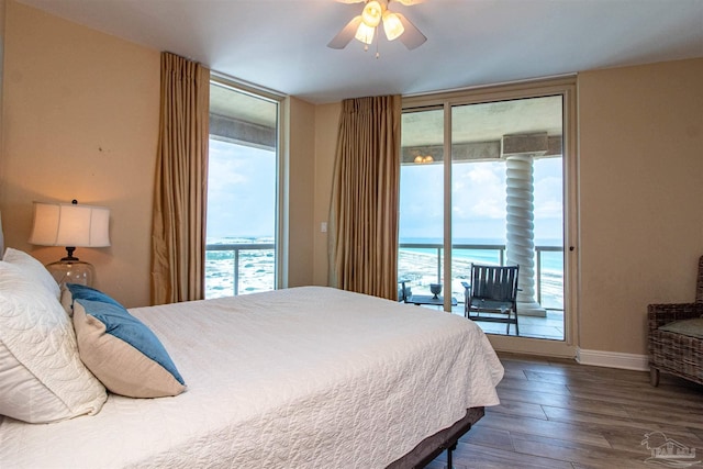 bedroom with hardwood / wood-style floors, a water view, access to outside, a wall of windows, and ceiling fan