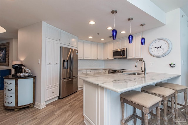 kitchen with sink, light wood-type flooring, stainless steel appliances, kitchen peninsula, and pendant lighting