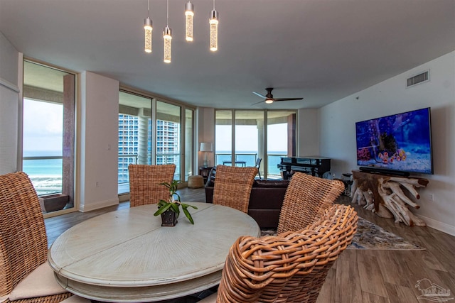 dining room with a wall of windows, ceiling fan, a water view, and hardwood / wood-style flooring