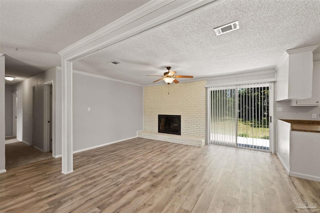 unfurnished living room featuring a brick fireplace, ceiling fan, light wood-type flooring, and a textured ceiling