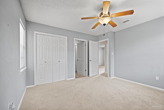 unfurnished bedroom featuring a textured ceiling, ceiling fan, a closet, and light colored carpet