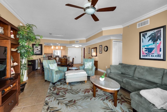 living area featuring light tile patterned floors, baseboards, visible vents, ceiling fan, and ornamental molding