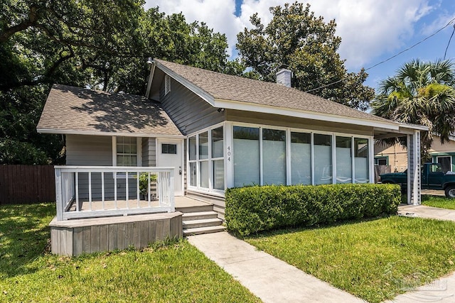 view of front of property with a porch, a shingled roof, a sunroom, a chimney, and a front yard