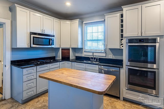 kitchen featuring stainless steel appliances, a kitchen island, a sink, wooden counters, and ornamental molding