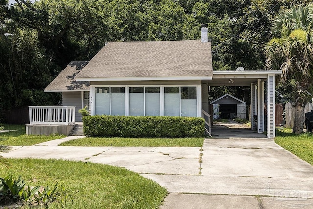 view of front of property with a shingled roof, concrete driveway, a chimney, an outbuilding, and a porch