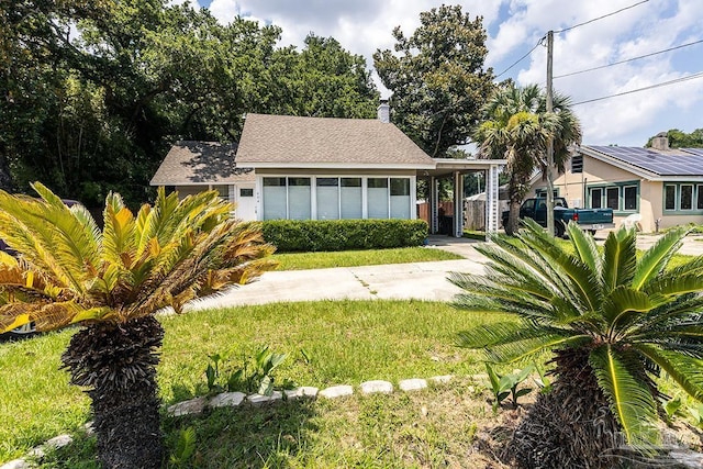 view of front of property featuring a carport, a front yard, concrete driveway, and roof with shingles