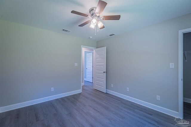 unfurnished bedroom featuring a closet, ceiling fan, a spacious closet, and dark hardwood / wood-style floors