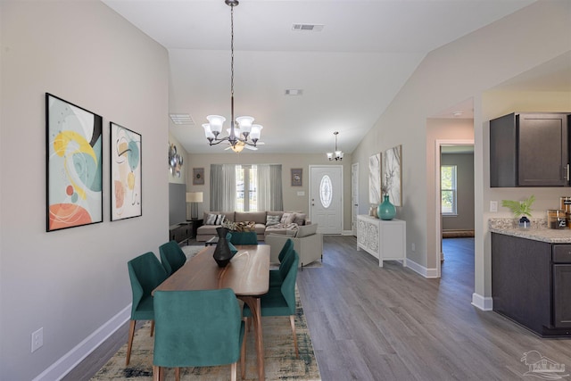 dining area with an inviting chandelier, vaulted ceiling, and light hardwood / wood-style floors