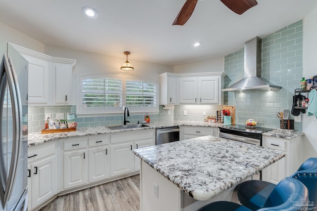 kitchen with wall chimney range hood, sink, a breakfast bar area, white cabinets, and light hardwood / wood-style floors