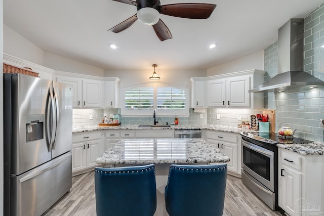 kitchen with ceiling fan, wall chimney range hood, appliances with stainless steel finishes, and white cabinets