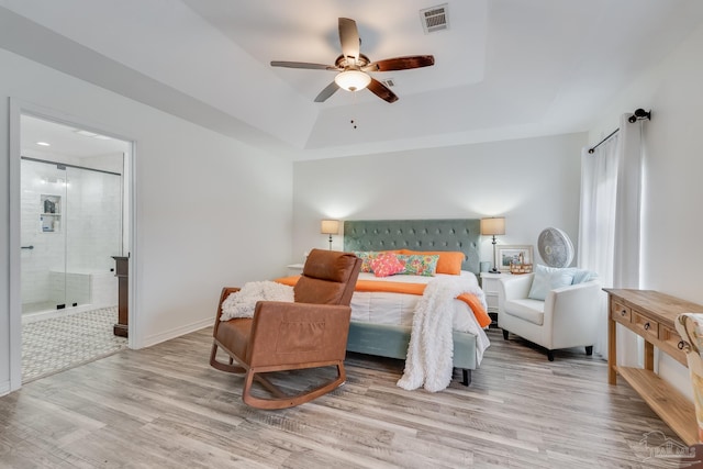 bedroom with a tray ceiling, ceiling fan, ensuite bathroom, and light hardwood / wood-style flooring