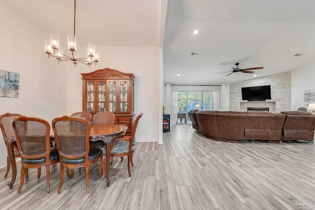 dining area with light wood-type flooring, ceiling fan with notable chandelier, and a fireplace