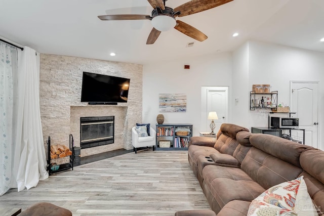 living room with lofted ceiling, a stone fireplace, ceiling fan, and light hardwood / wood-style floors