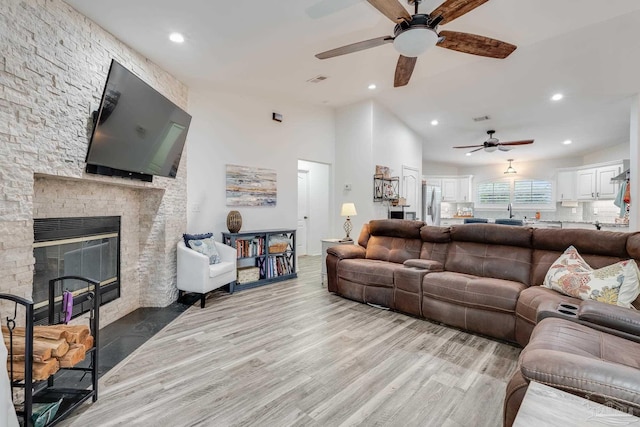 living room featuring light hardwood / wood-style floors, ceiling fan, lofted ceiling, and a fireplace