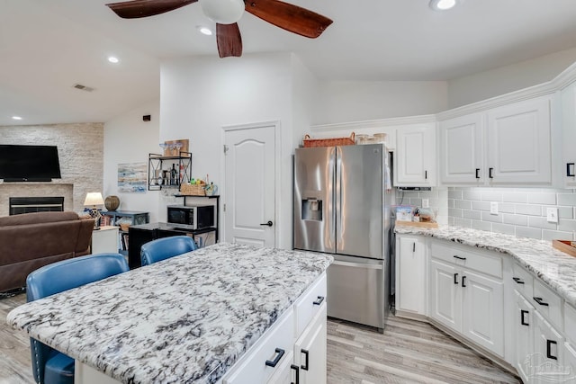 kitchen featuring white cabinetry, light hardwood / wood-style flooring, ceiling fan, a stone fireplace, and appliances with stainless steel finishes