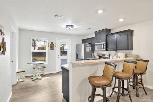 kitchen with light countertops, appliances with stainless steel finishes, light wood-style floors, a peninsula, and a kitchen breakfast bar