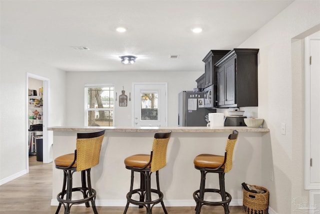 kitchen featuring a breakfast bar, visible vents, light countertops, fridge, and light wood finished floors