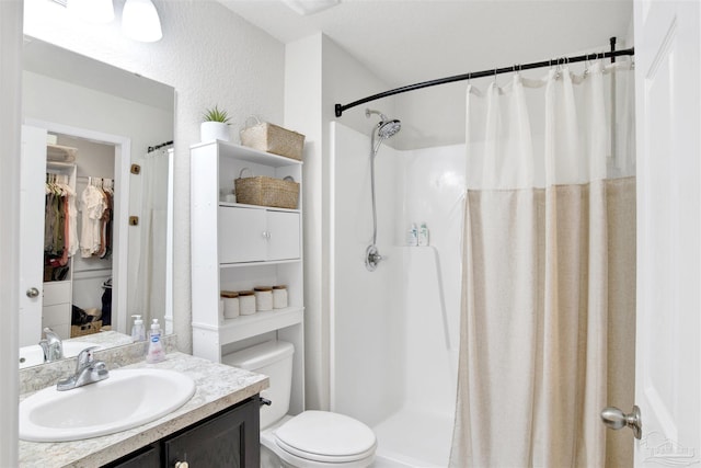 bathroom with a textured wall, a stall shower, vanity, and toilet