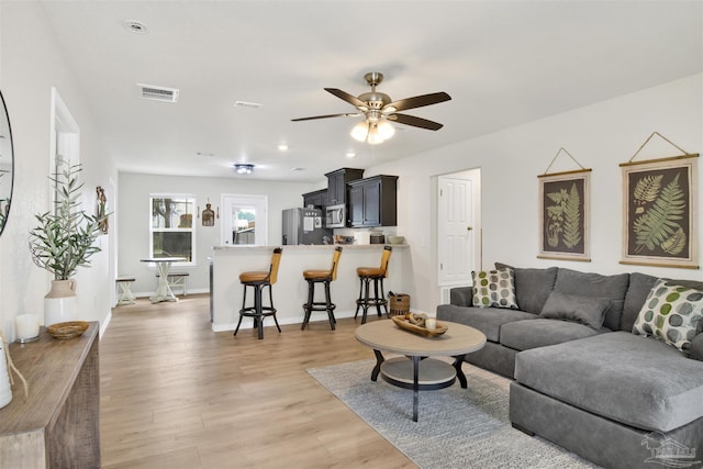 living area with ceiling fan, light wood-style flooring, visible vents, and baseboards